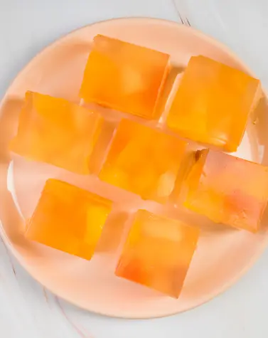 Orange jelly cubes made with agar agar on a peach plate, showcasing vegan dessert texture