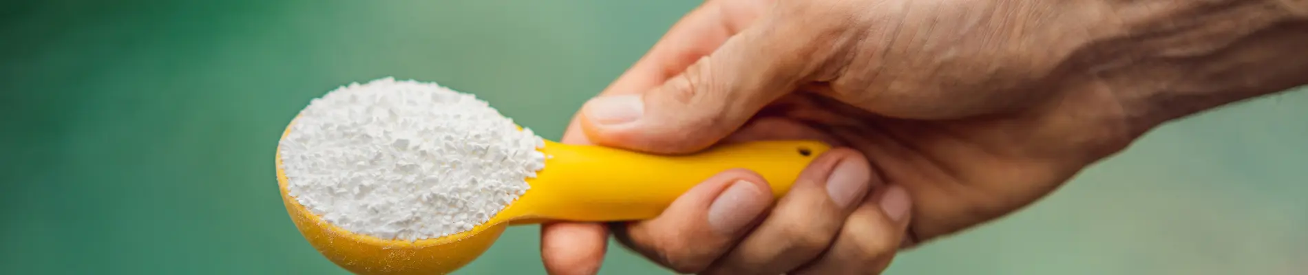 White Gellan Gum powder in yellow scoop held by hand with green background