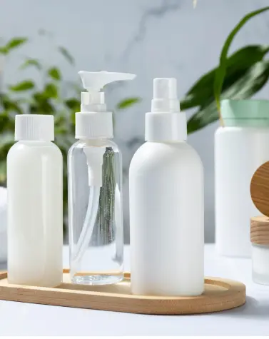 Collection of white and transparent cosmetic bottles containing guar gum formulations displayed on a wooden tray against a marble background with green plants