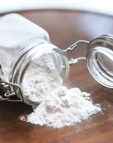 Glass jar spilling white Gellan Gum powder on wooden surface