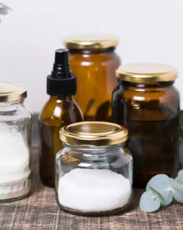 Glass jars and amber bottles with natural skincare ingredients on a wooden surface, representing clean beauty and cationic guar gum in cosmetic formulations.