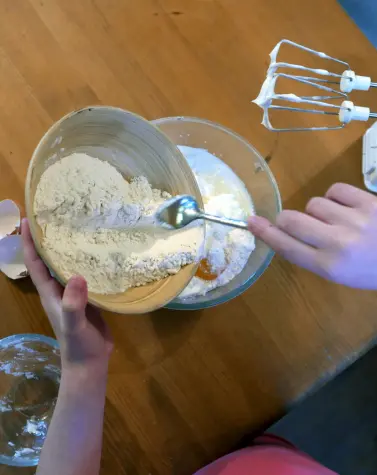Person adding food thickener to a mixing bowl with eggs and sugar, illustrating the use of food thickeners in baking.