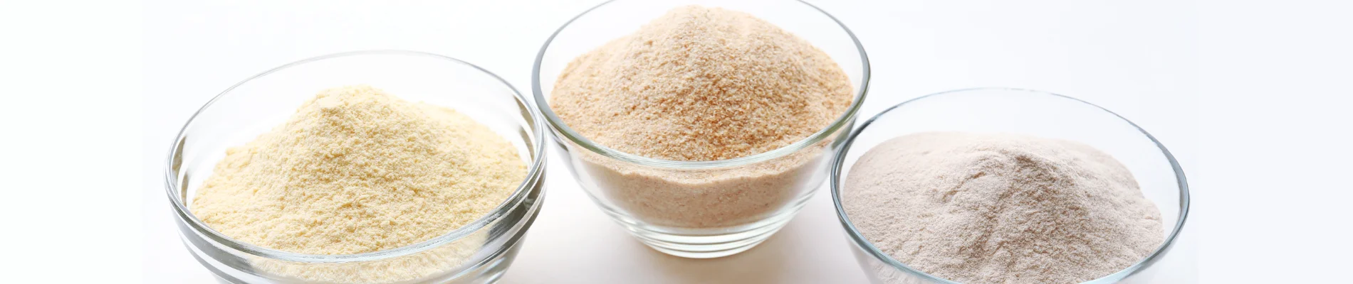 Three glass bowls with yellow, light brown, and white food additive powders used in processed foods.