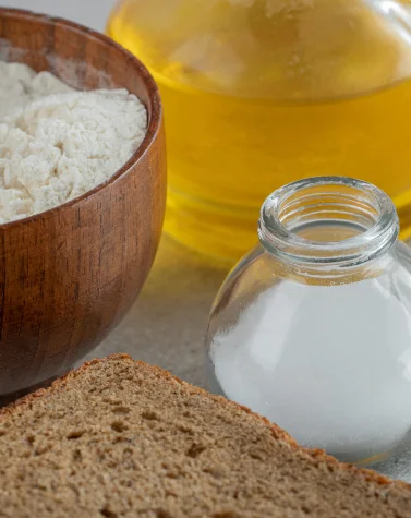 Different forms of food additives including powder form in a wooden bowl, liquid form in a glass bottle, solid form in a small jar, and brown bread.