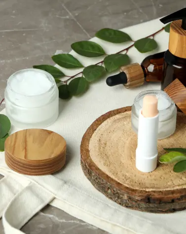 Eco-friendly skincare products including cream, dropper bottle, and lip balm on wooden surface with green leaves, representing sustainable beauty