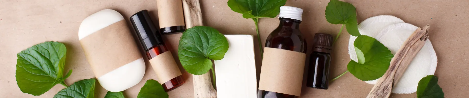 Natural skincare products with brown labels, soap bars, and cotton pads on brown surface with green leaves—representing sustainable beauty formulations