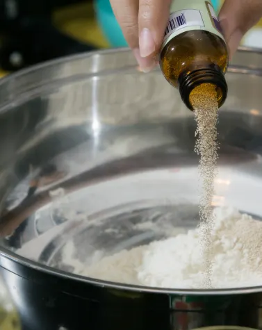 Person adding food stabilizer from a brown bottle into a bowl of flour.