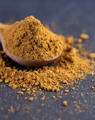 Cassia powder in a wooden spoon with spilled powder around it, showcasing its fine texture and natural appearance.