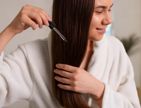 Applying dropper serum conditioner to long hair for conditioning and smoothness in hair care routine.