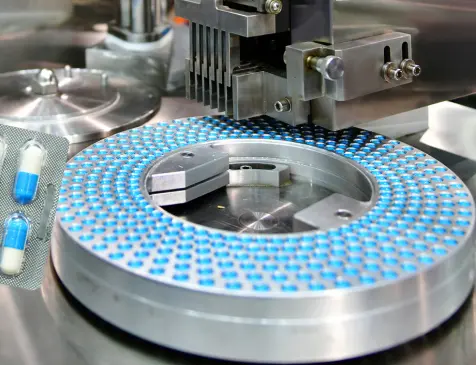 Rotary tablet press compressing blue-and-white pharmaceutical tablets, demonstrating the tablet binding process in a clean manufacturing facility.